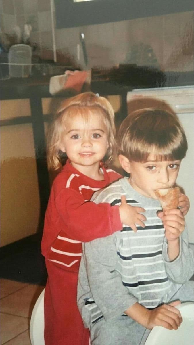 Two small children in a kitchen, one hugging the other from behind