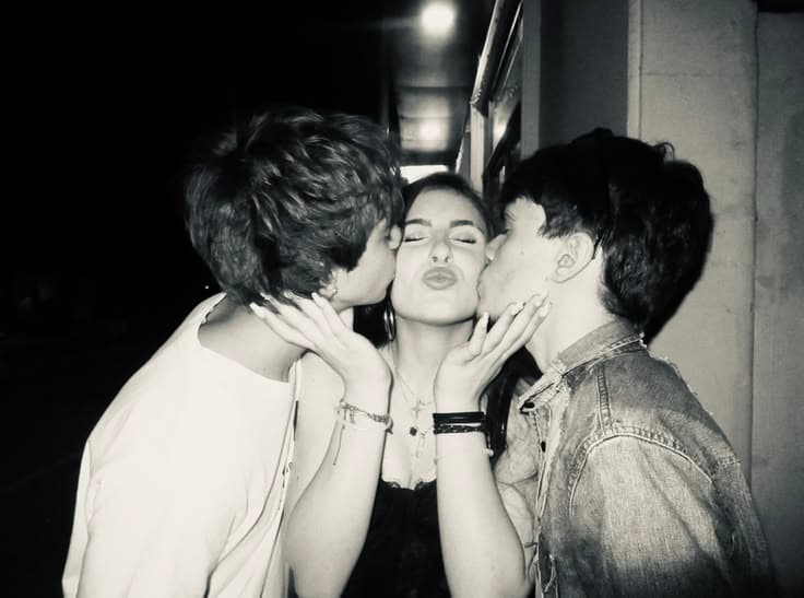 Two friends kissing a girl on both cheeks at night
